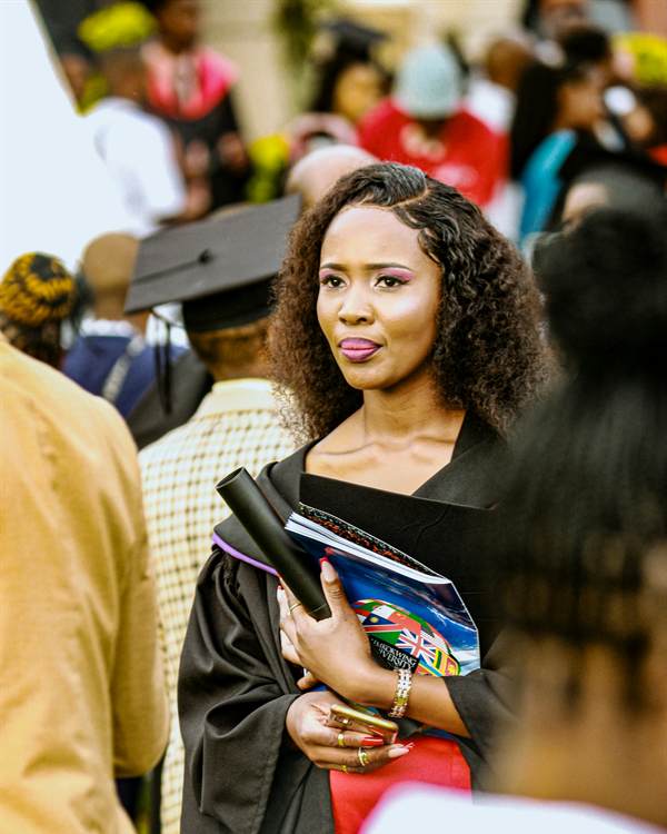 Jeune diplômée en toge tenant ses livres et son diplôme