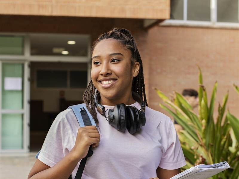 Étudiante souriante sur un campus, ses livres à la main